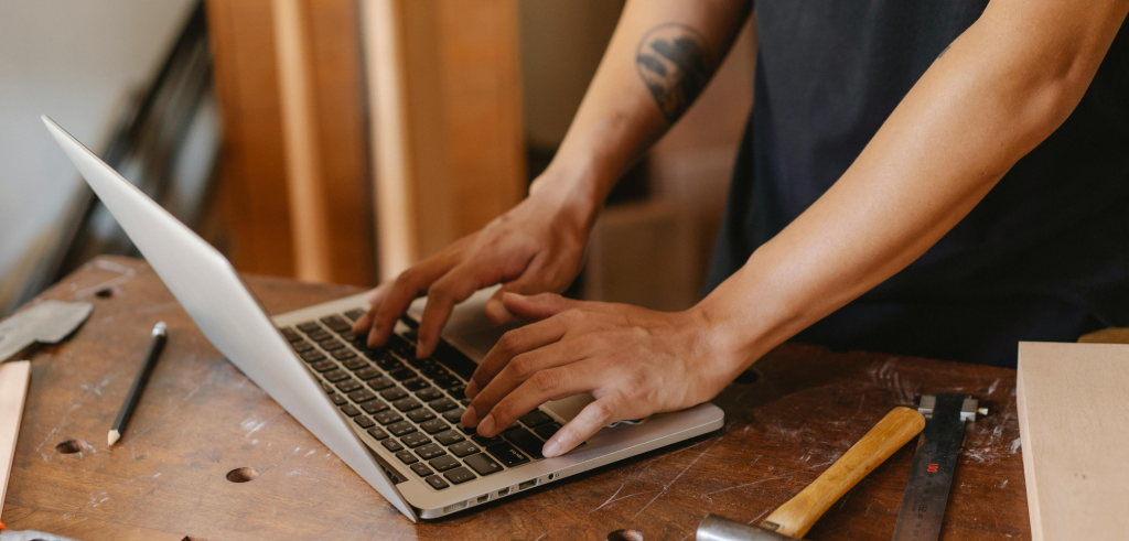 Tradesperson using a laptop in a workshop to manage client quotes and service reports